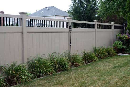 Tan vinyl privacy fence installed in a landscaped backyard